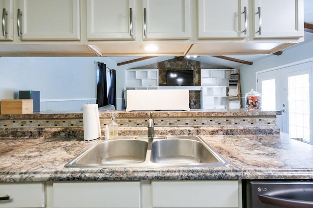 kitchen with sink, dishwasher, white cabinetry, dark stone countertops, and lofted ceiling with beams