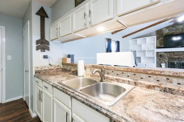 kitchen with lofted ceiling, sink, white cabinetry, dark hardwood / wood-style flooring, and a fireplace