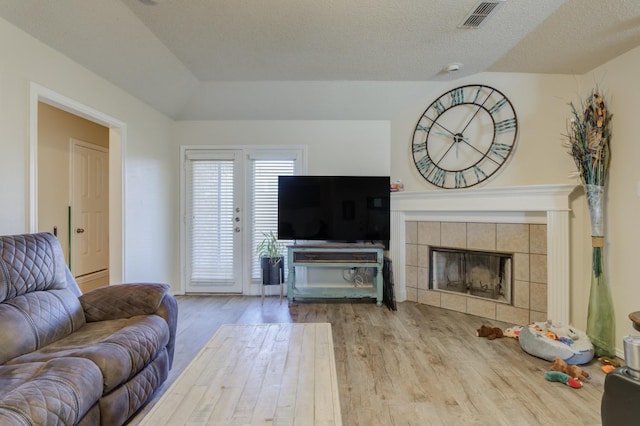 living room with a tiled fireplace, light hardwood / wood-style flooring, and a textured ceiling