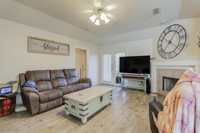 living room featuring ceiling fan, a fireplace, light hardwood / wood-style floors, and a textured ceiling