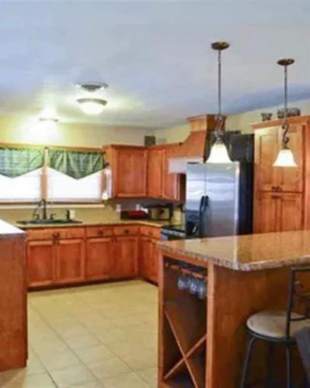 kitchen featuring a kitchen bar, stainless steel fridge, sink, and hanging light fixtures