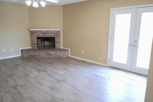 unfurnished living room with a fireplace, french doors, ceiling fan, and light wood-type flooring