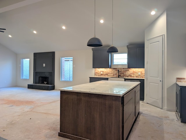 kitchen with a large fireplace, a kitchen island, backsplash, vaulted ceiling, and a sink