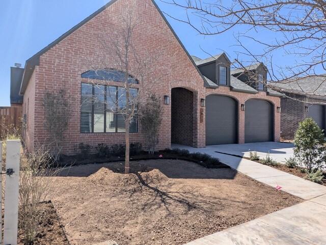 french country home with a garage, roof with shingles, concrete driveway, and brick siding