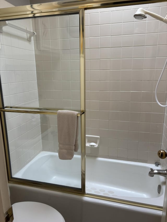 bathroom featuring bath / shower combo with glass door and toilet