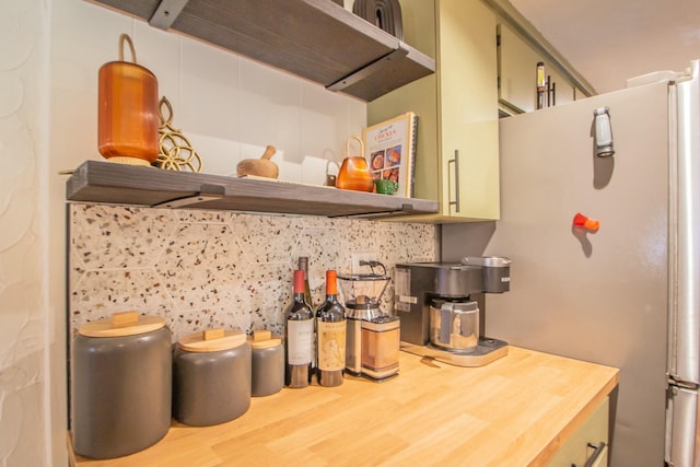 kitchen with butcher block countertops, decorative backsplash, range hood, freestanding refrigerator, and wood finished floors