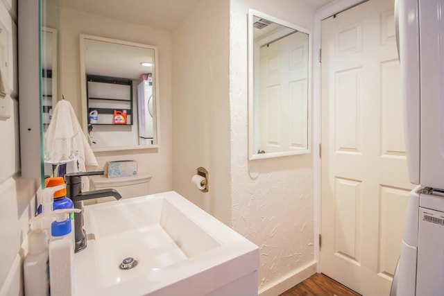 bathroom featuring baseboards, a textured wall, stacked washing maching and dryer, wood finished floors, and a sink