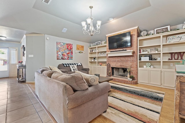 living room with a brick fireplace, an inviting chandelier, light wood-type flooring, and a tray ceiling