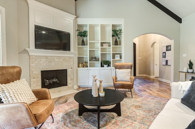 living room featuring vaulted ceiling with beams, light hardwood / wood-style flooring, and a brick fireplace