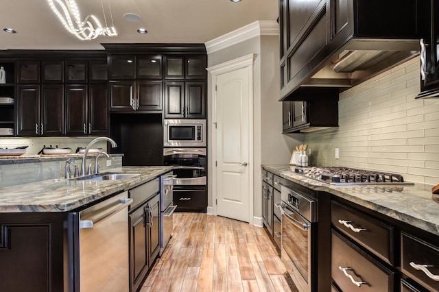 kitchen with appliances with stainless steel finishes, sink, hanging light fixtures, crown molding, and light wood-type flooring