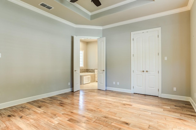 unfurnished bedroom with crown molding, a raised ceiling, a closet, and light wood-type flooring