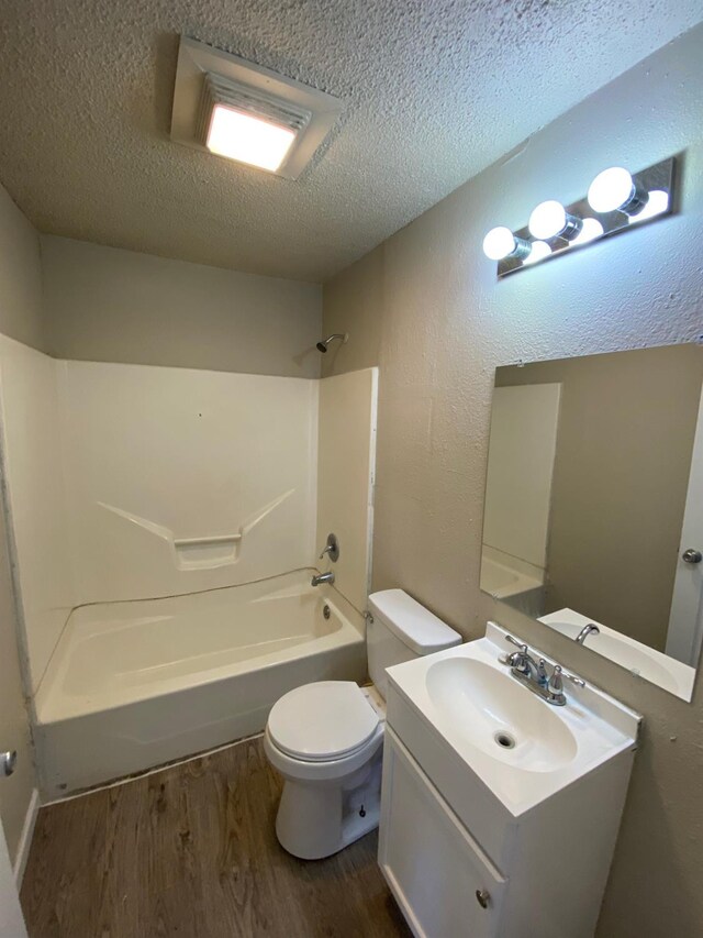 full bathroom with shower / tub combination, vanity, wood-type flooring, a textured ceiling, and toilet