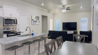 kitchen with a breakfast bar area, white cabinetry, open floor plan, a ceiling fan, and appliances with stainless steel finishes