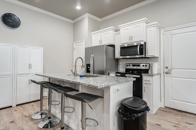 kitchen with light wood-style flooring, light stone counters, crown molding, a center island with sink, and appliances with stainless steel finishes