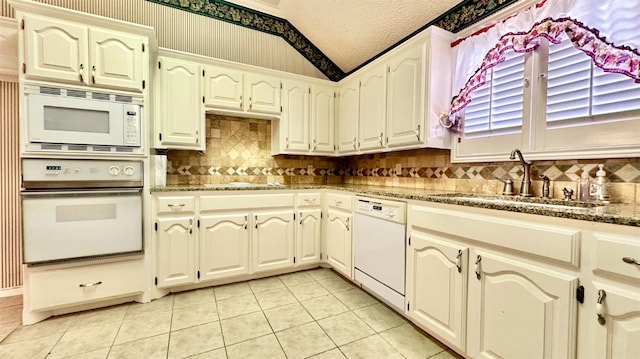 kitchen with sink, vaulted ceiling, a textured ceiling, white appliances, and light stone countertops