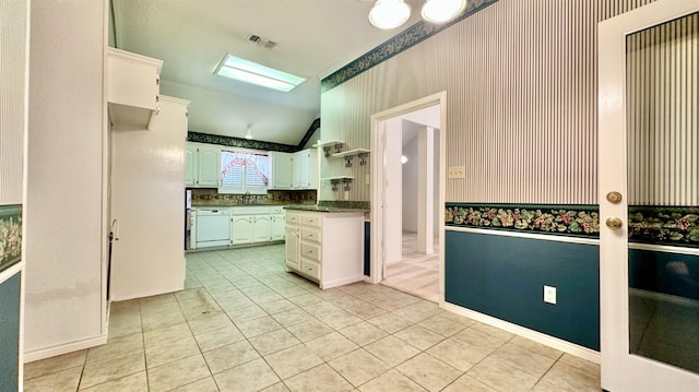 kitchen with light tile patterned flooring, lofted ceiling, sink, white cabinets, and white dishwasher