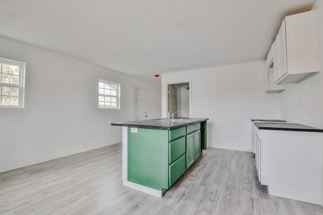 kitchen with sink, an island with sink, green cabinetry, white cabinets, and light wood-type flooring