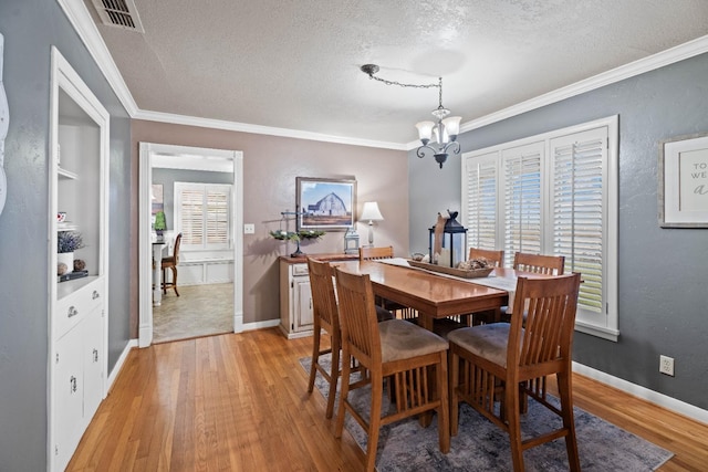 dining area with crown molding, an inviting chandelier, a textured ceiling, light wood-type flooring, and built in features