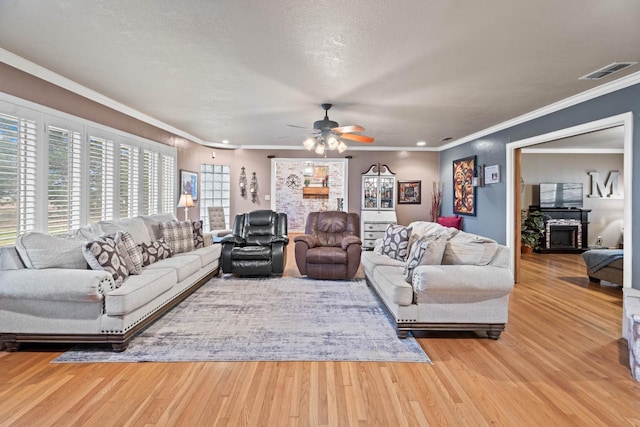 living room featuring ceiling fan, ornamental molding, light hardwood / wood-style flooring, and a textured ceiling