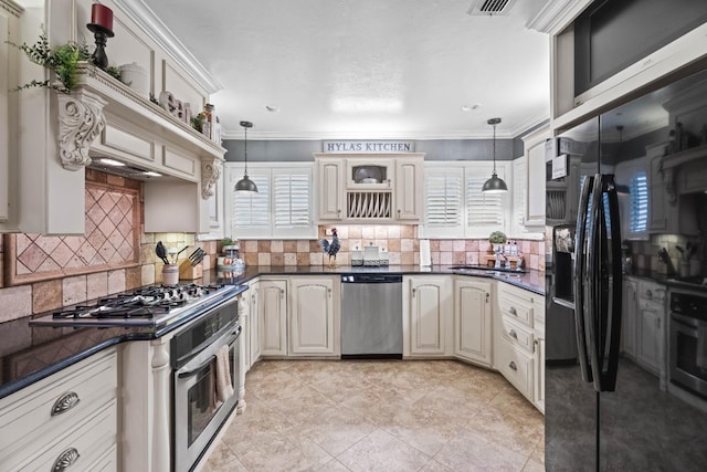 kitchen with stainless steel appliances, decorative backsplash, cream cabinetry, and decorative light fixtures