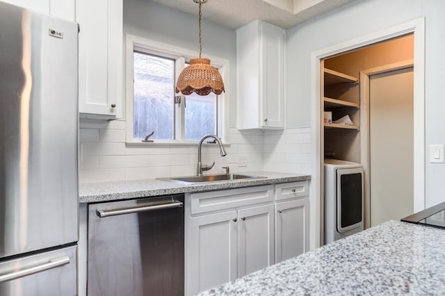 kitchen featuring sink, hanging light fixtures, appliances with stainless steel finishes, washer / clothes dryer, and white cabinets