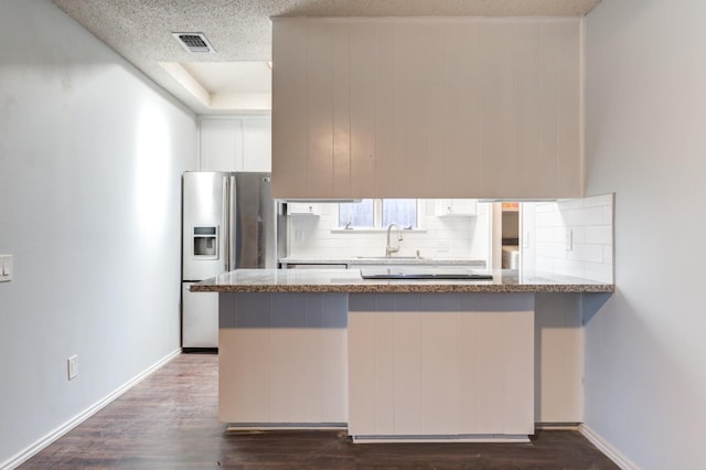 kitchen with dark hardwood / wood-style floors, white cabinets, stainless steel fridge, backsplash, and kitchen peninsula