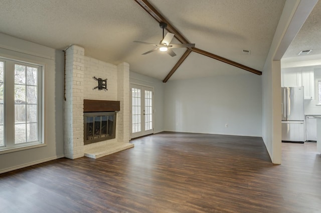 unfurnished living room with a fireplace, lofted ceiling with beams, dark hardwood / wood-style flooring, plenty of natural light, and a textured ceiling