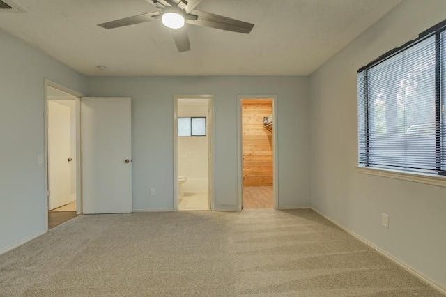 unfurnished bedroom with light carpet, ensuite bath, ceiling fan, and a spacious closet