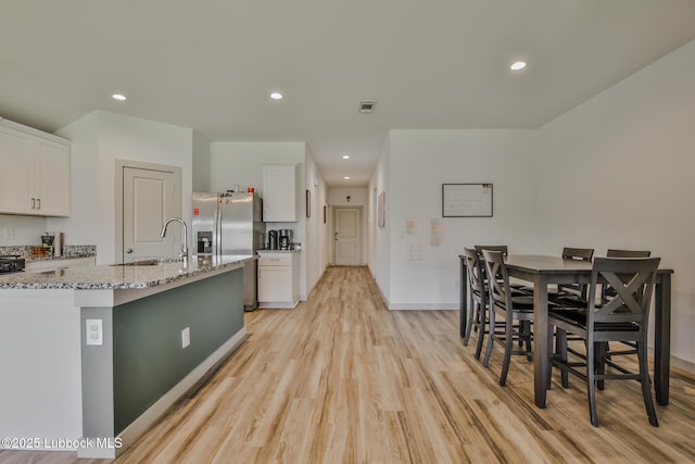 7406 9th St, Lubbock, TX 79416 - kitchen featuring a sink, stainless steel refrigerator with ice dispenser, white cabinets, light wood-style floors, and light stone countertops