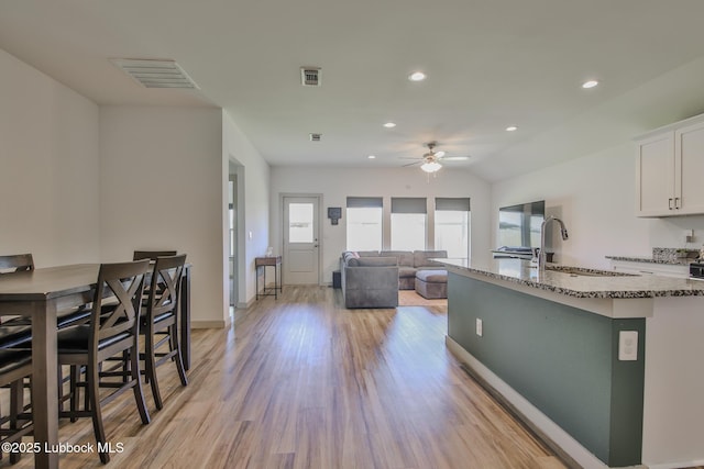 7406 9th St, Lubbock, TX 79416 - kitchen with a ceiling fan, light stone counters, a sink, white cabinetry, and light wood-style floors