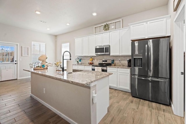 kitchen with sink, appliances with stainless steel finishes, an island with sink, light stone countertops, and white cabinets