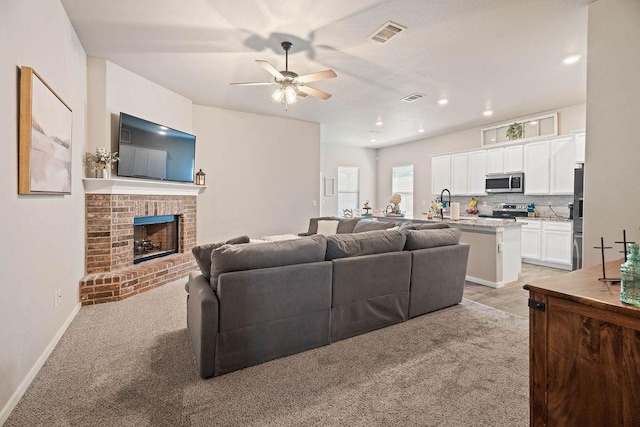 carpeted living room with ceiling fan, a fireplace, and sink