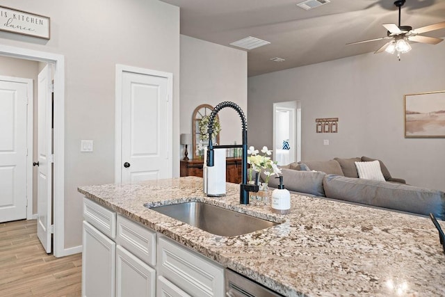 kitchen with sink, ceiling fan, light stone counters, light hardwood / wood-style floors, and white cabinets