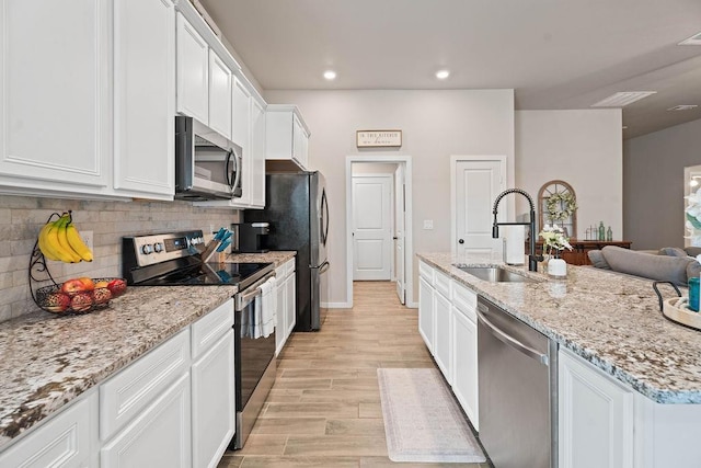 kitchen with appliances with stainless steel finishes, white cabinetry, sink, light stone counters, and light hardwood / wood-style flooring