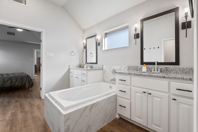 bathroom featuring vanity, hardwood / wood-style flooring, vaulted ceiling, and tiled bath