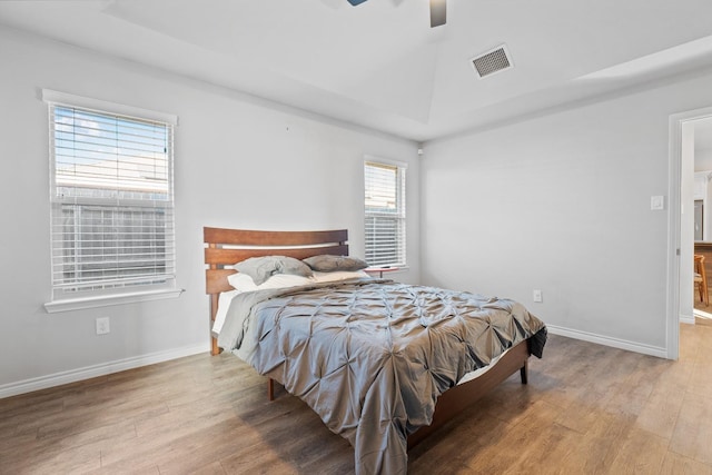 bedroom with ceiling fan, a tray ceiling, and light wood-type flooring