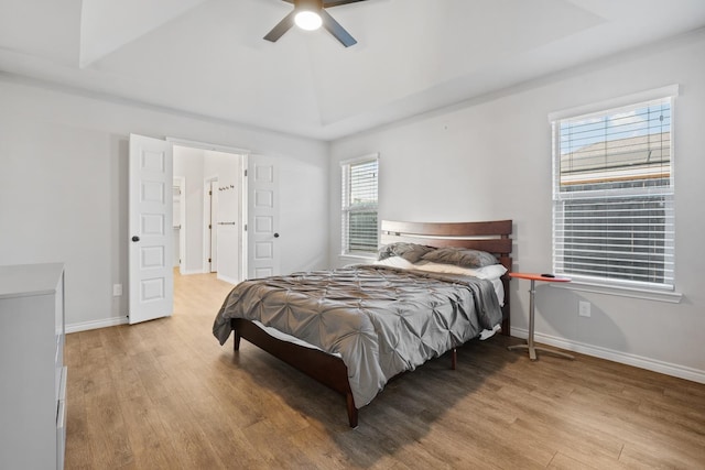 bedroom featuring ceiling fan, a tray ceiling, and light hardwood / wood-style flooring