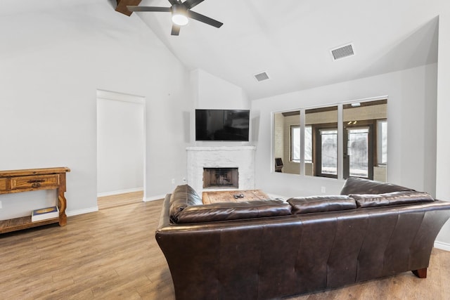 living room featuring vaulted ceiling with beams, a high end fireplace, ceiling fan, and light wood-type flooring