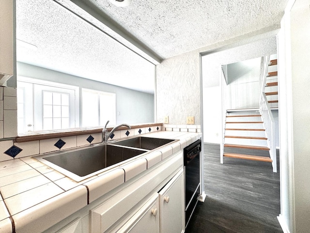 kitchen with sink, a textured ceiling, dark hardwood / wood-style flooring, tile counters, and black dishwasher