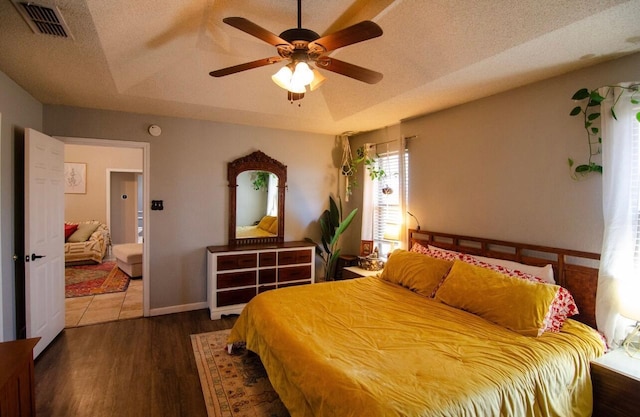 bedroom featuring wood finished floors, visible vents, a ceiling fan, a textured ceiling, and a tray ceiling