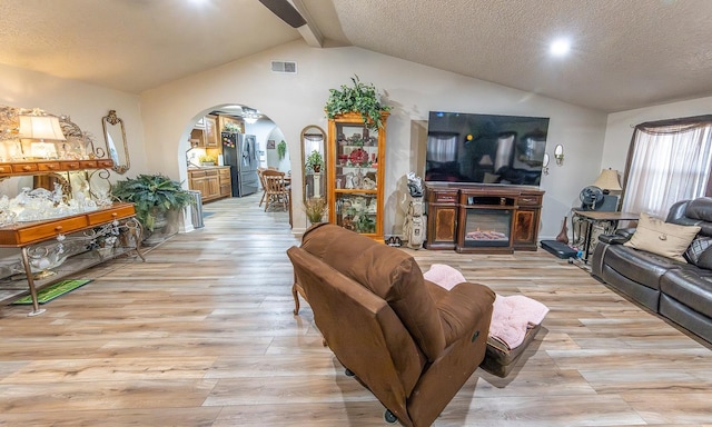 living room featuring a fireplace, light hardwood / wood-style flooring, lofted ceiling with beams, and a textured ceiling