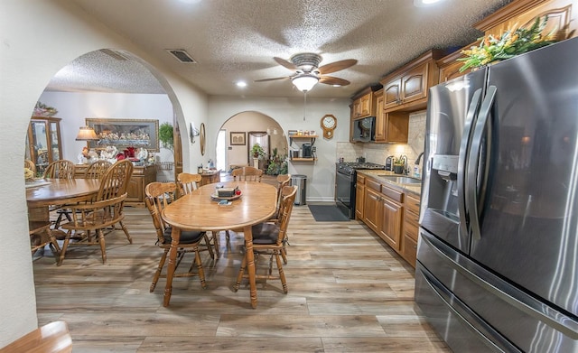 dining area featuring ceiling fan, sink, a textured ceiling, and light hardwood / wood-style flooring