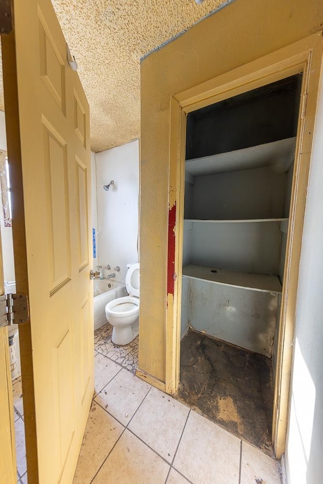 bathroom with tile patterned flooring, a tub to relax in, a textured ceiling, and toilet