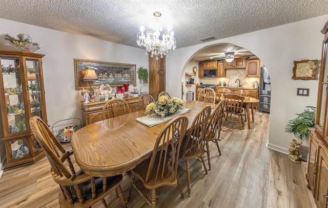 dining room with an inviting chandelier, sink, a textured ceiling, and light wood-type flooring