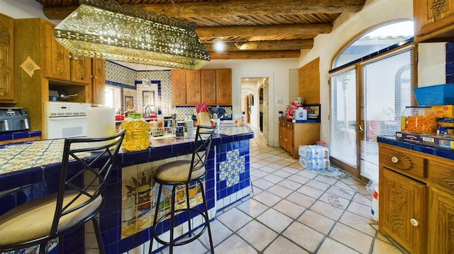 kitchen with light tile patterned flooring, decorative backsplash, tile counters, white oven, and beam ceiling