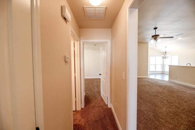 corridor featuring lofted ceiling, a chandelier, and dark carpet