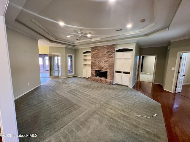 9802 Toledo Ave, Lubbock, TX 79424 - unfurnished living room with a tray ceiling, a ceiling fan, a brick fireplace, dark wood-type flooring, and crown molding