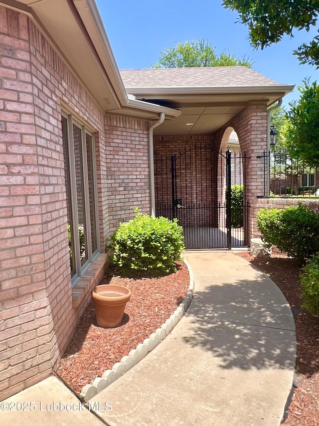 9802 Toledo Ave, Lubbock, TX 79424 - view of exterior entry featuring brick siding, a gate, and a shingled roof