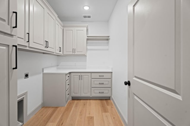 washroom with electric dryer hookup, cabinets, and light wood-type flooring