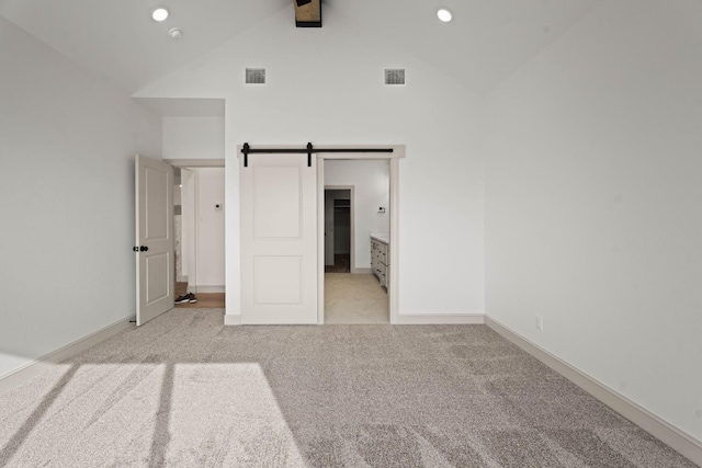 unfurnished bedroom with light carpet, high vaulted ceiling, and a barn door